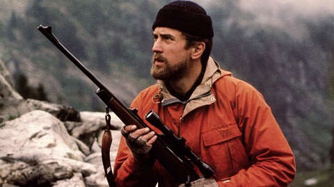 Man in orange coat holding hunting rifle in wilderness